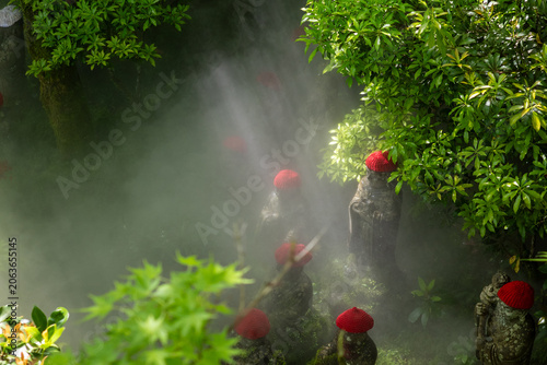 Stone Jizo statues with red hats surrounded by mist and green foliage, Japan