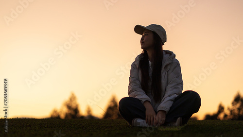 Фотография Young woman sitting on grass at sunset, reflecting in a peaceful outdoor moment
