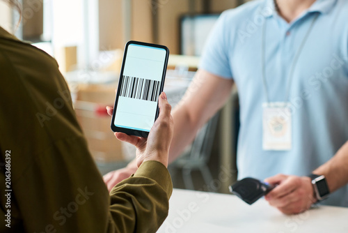 Billede på lærred Close up of young woman showing smartphone barcode at order pickup counter while male worker scanning payment device