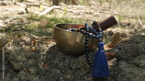 Tibetan singing bowl with rosary mala on a rock in a garden with green background