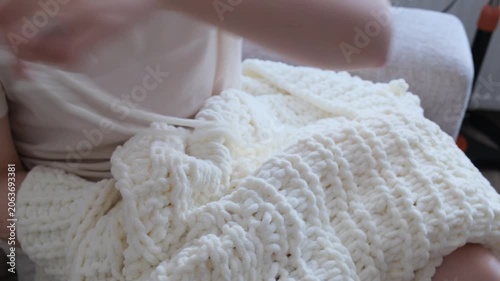 Close up of female hands knitting a cozy, soft white cardigan using chunky plush loop yarn at home.