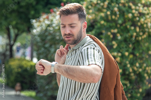 Valokuva Young man looking at his wristwatch in the city