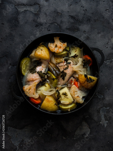 Slow cooking chicken with seasonal vegetables in a cast-iron skillet on a dark background, top view. Simple, comfort food