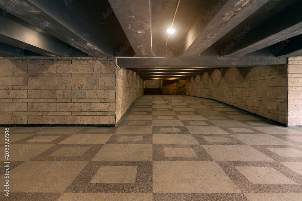 Fototapeta premium Illuminated underground pedestrian tunnel with patterned floor and stone walls