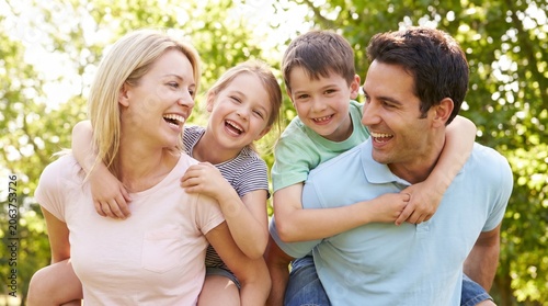 Happy Parents Giving Piggyback Rides to Their Young Children in a Sunny Green Park During a Weekend Outing