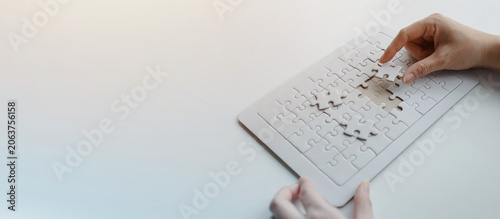 Photography Hands completing a white puzzle board by placing the missing piece, illustrating problem solving, logical thinking, teamwork, strategic planning, and achieving complete business solutions