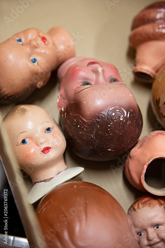 Collection of vintage doll heads scattered in a cardboard box, some with chipped paint