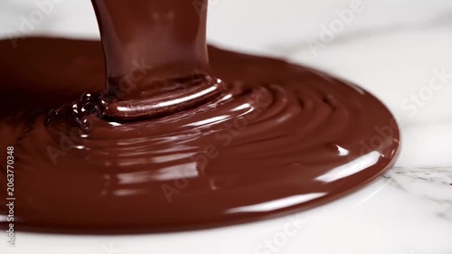 Close-up of rich, melted dark chocolate being poured, creating beautiful swirls on a marble surface