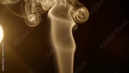 Wisps of golden smoke curl elegantly against a dark background, creating an ethereal and atmospheric visual