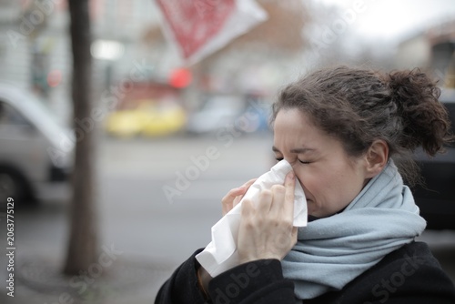Sick woman blowing her nose with a tissue outside
