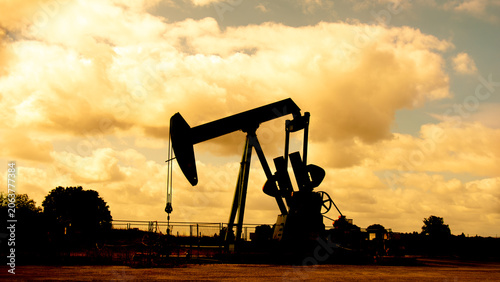 Chevalet de pompage en silhouette sur un arrière plan de nuages au soleil couchant. Exploitation d'un puits de pétrole et extraction du pétrole brut. Concepts de prix du pétrole et crise énergétique