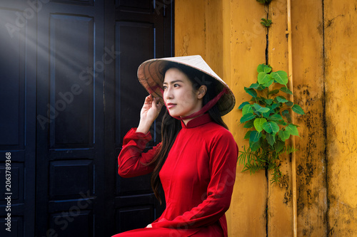 A young Vietnamese woman wearing a traditional Ao Dai dress is sightseeing in Hoi An, Vietnam.