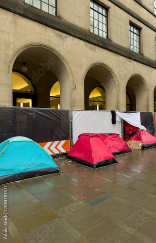 Tents and Homeless Encampment Outside Stone Arched Building in Urban Street Scene