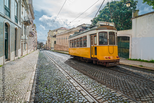 Iconic yellow tram traveling on a historic cobblestone street through the charming city center of Lisbon, depicting traditional public transportation and urban life