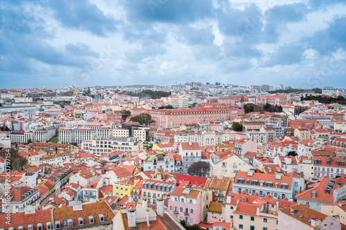Lisbon cityscape presenting a high angle panoramic view of densely packed historic buildings. Featuring a vibrant array of traditional red tiled roofs. Colorful facades