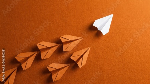 Single white paper airplane leading orange paper airplanes on orange background showcasing leadership concept.