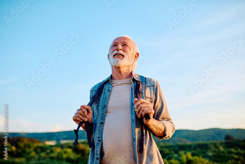 Tableau sur toile Happy senior man smiling while holding backpack straps, enjoying active retireme