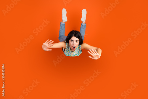 Tablou pe pânză Top view of a young woman showing surprise on a vibrant orange background, empha