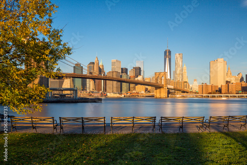 Brooklyn Bridge and Lower Manhattan skyline viewed from an empty park waterfront, featuring autumn foliage and copy space for urban tourism and travel advertising, New York City, USA.