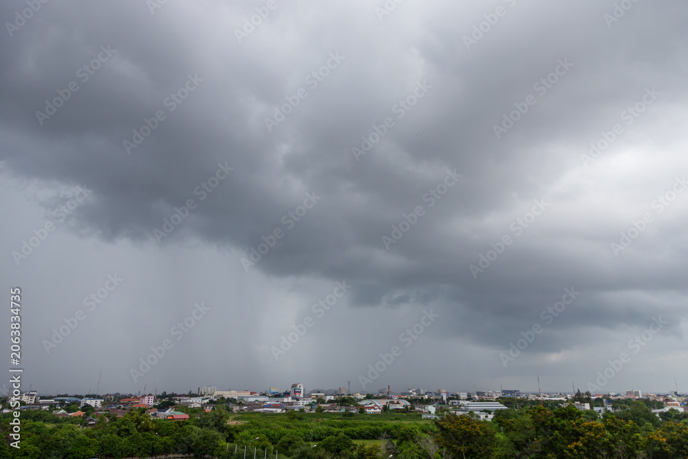 Fototapeta premium A high angle view overlooking a green, tree filled area and a city skyline, with heavy rain falling from dark, dramatic storm clouds.