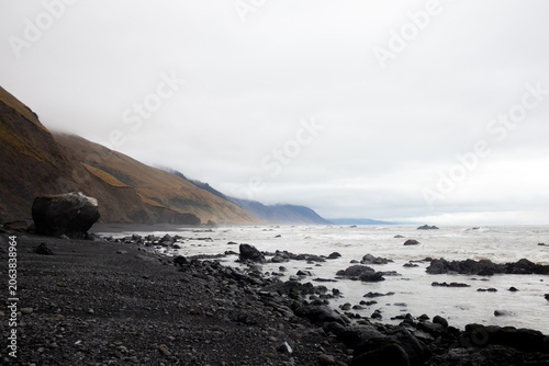 View of the rugged Lost Coast featuring a black sand beach, large boulders, and steep hills under an overcast sky in Humboldt County, California, United States.