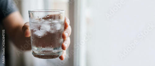 Person's hand carrying a glass of water filled with ice cubes, showing condensation for a cool drink