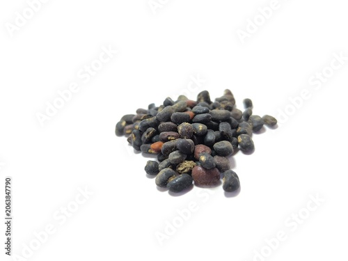 Fotografie A small pile of raw, unpolished black beans or dark plant seeds mixed with occasional reddish-brown grains, shot from a slightly elevated eye-level perspective, isolated on a clean white background