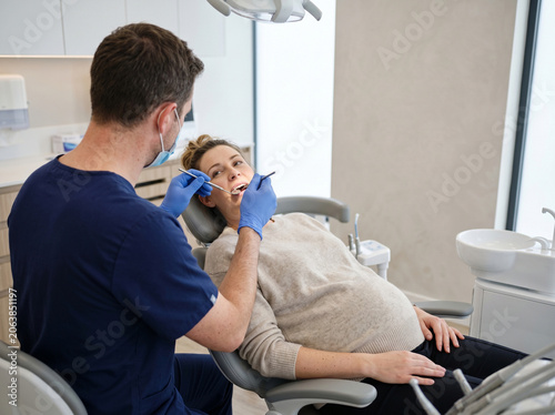 Male dentist examining pregnant woman patient in modern clinic
