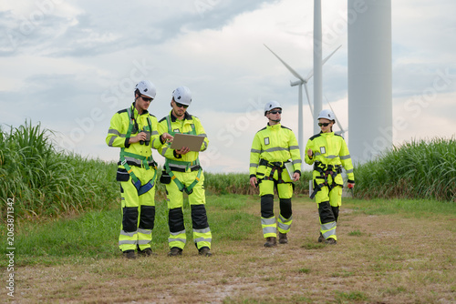 Caucasian male engineer reviewing turbine performance report on tablet while crew observes, safety uniform, outdoor maintenance for renewable electricity generation, future energy teamwork project