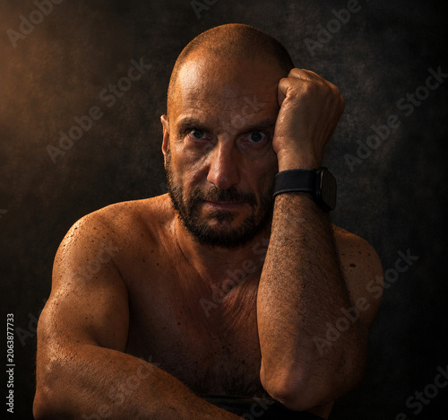 Dramatic portrait of a bald mature man with muscular physique against dark background
