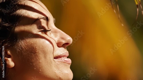 Woman relaxing in sunlight outdoors. Extreme close-up of female face with shadows on skin. Wellness and skincare concept, natural lighting for beauty industry