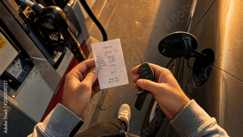 Refuel fuel gasstation pump car receipt keys driver payment sunset scene showing a driver holding receipt and car keys beside a pump during golden hour with warm light and blurred road background