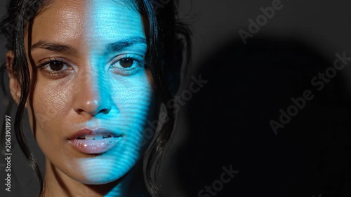 Woman with blue abstract light pattern on face. Portrait of attractive lady illuminated by projection. Futuristic cyber digital technology and security concept
