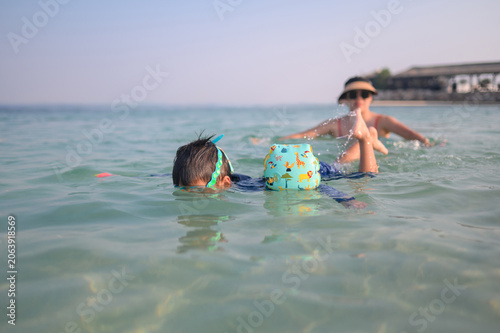 Child Swimming with Mother in Clear Water at Beach on Sunny Day