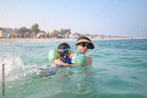 Asian woman in sunglasses carries multiracial son in water at be