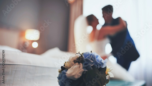 Bridal bouquet with soft focus silhouette of bride and groom in a romantic room.