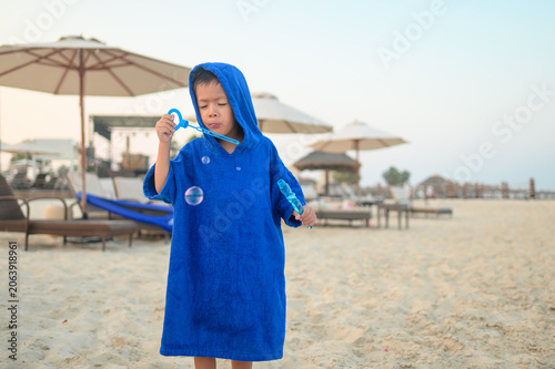 Four-Year-Old Boy in Blue Towel Playing with Bubbles on Beach at