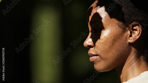 African american woman profile view in sunlight. Face of lady with leaf shadows cast on skin. Natural lighting portrait outdoors in garden for beauty concept