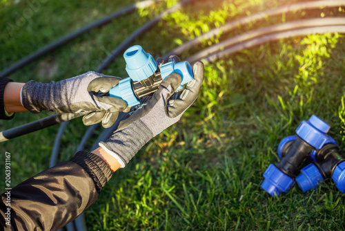 Closeup of hands in the gloves. Process of installing fittings pipes and connectors for the garden and lawn irrigation system installation. Green grass, shallow depth of field.