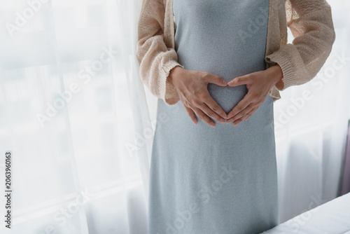 Fotografie Young asian pregnant woman touching her belly at home