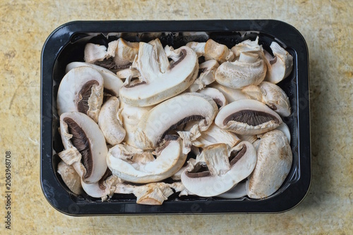 A pile of sliced ​​white fresh champignon mushrooms in a black box on a brown table in the kitchen