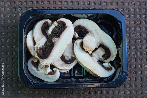 A pile of sliced ​​white fresh champignon mushrooms in a black box on a brown table in the kitchen