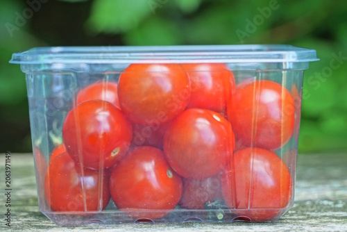 red round fresh tomatoes  in a white plastic box stands on a gray brown wooden table