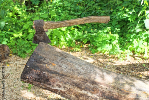 one big old brown axe sticks out of a piece of cut log on the gray ground 