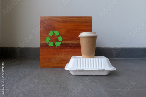 A takeaway paper cup and food container are placed in front of a wooden recycling bin with a green recycle symbol. Suitable for disposable waste, recycling, food packaging, sustainability