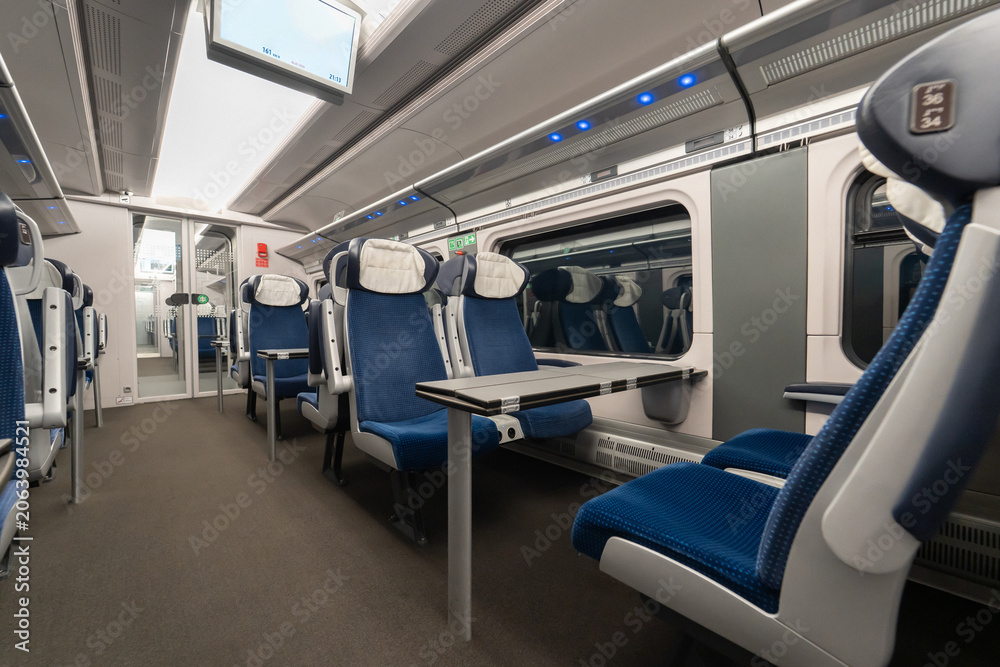 Obraz premium Empty interior of modern high speed train passenger carriage with blue seats and foldable tables. Clean cabin of intercity express for travel commute transportation tourism business trip.