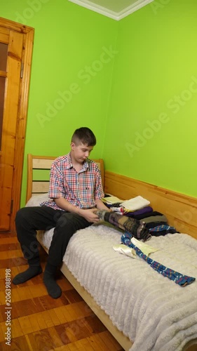 A boy sits on the bed folding clothes, organizing his room and neatly arranging items around him.