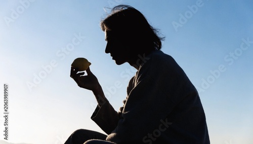 Striking silhouette of a person holding a bright ripe yellow lemon against a clean soft background highlighting themes of health, wellness, fresh organic food, and natural citrus nutrition.
