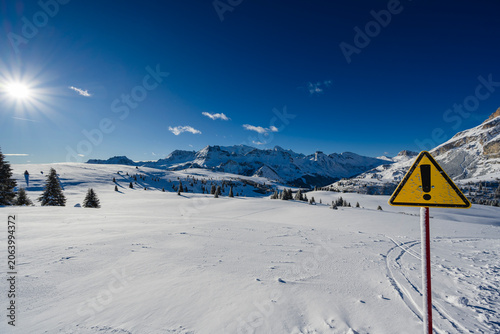 Snowy mountain landscape under clear blue sky with warning sign in the foreground.
