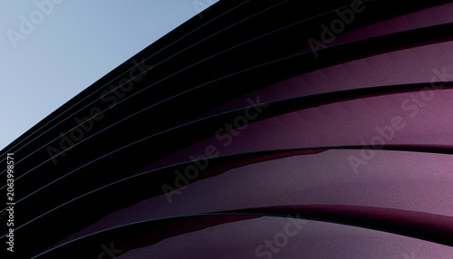 Curved abstract architectural structure with sleek purple and black lines against a clear sky.